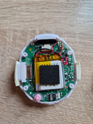 A tamagotchi smart with the back removed. Components such as the battery, speaker wires, PCB and chip are visible